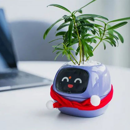 "A small purple Ai  plant pot with a digital face displaying a cheerful expression and a red scarf wrapped around it. The pot holds a green leafy plant on top, resembling hair. It is placed on a white table with a blurred laptop in the background, suggesting a modern indoor setting."