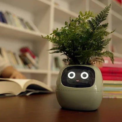 A small Ai  plant pot with a digital face displaying bright eyes and a small smile. The pot holds lush green ferns on top, resembling hair. It is placed on a wooden table with books and shelves in the blurred background, suggesting a cozy indoor environment.